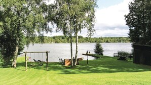 Nurmikkoalue, jossa on leikkikeinu ja laituri, joka ulottuu järveen. Alue on puuston ympäröimä.