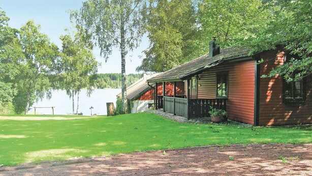 Tunnelmallinen mökki, jossa on puinen ulkoverhous, kuisti ja näkymä järvelle.