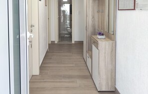 Un pasillo con piso de madera, un mueble de madera con un jarrón, y una puerta con un cartel.