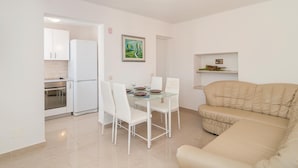 Un espacio habitable compacto con kitchenette, un comedor con mesa de vidrio y un sofá color beige.