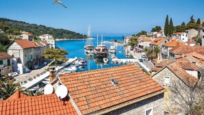 Un pueblo costero con edificios de piedra, un puerto deportivo con barcos y un cielo azul despejado.