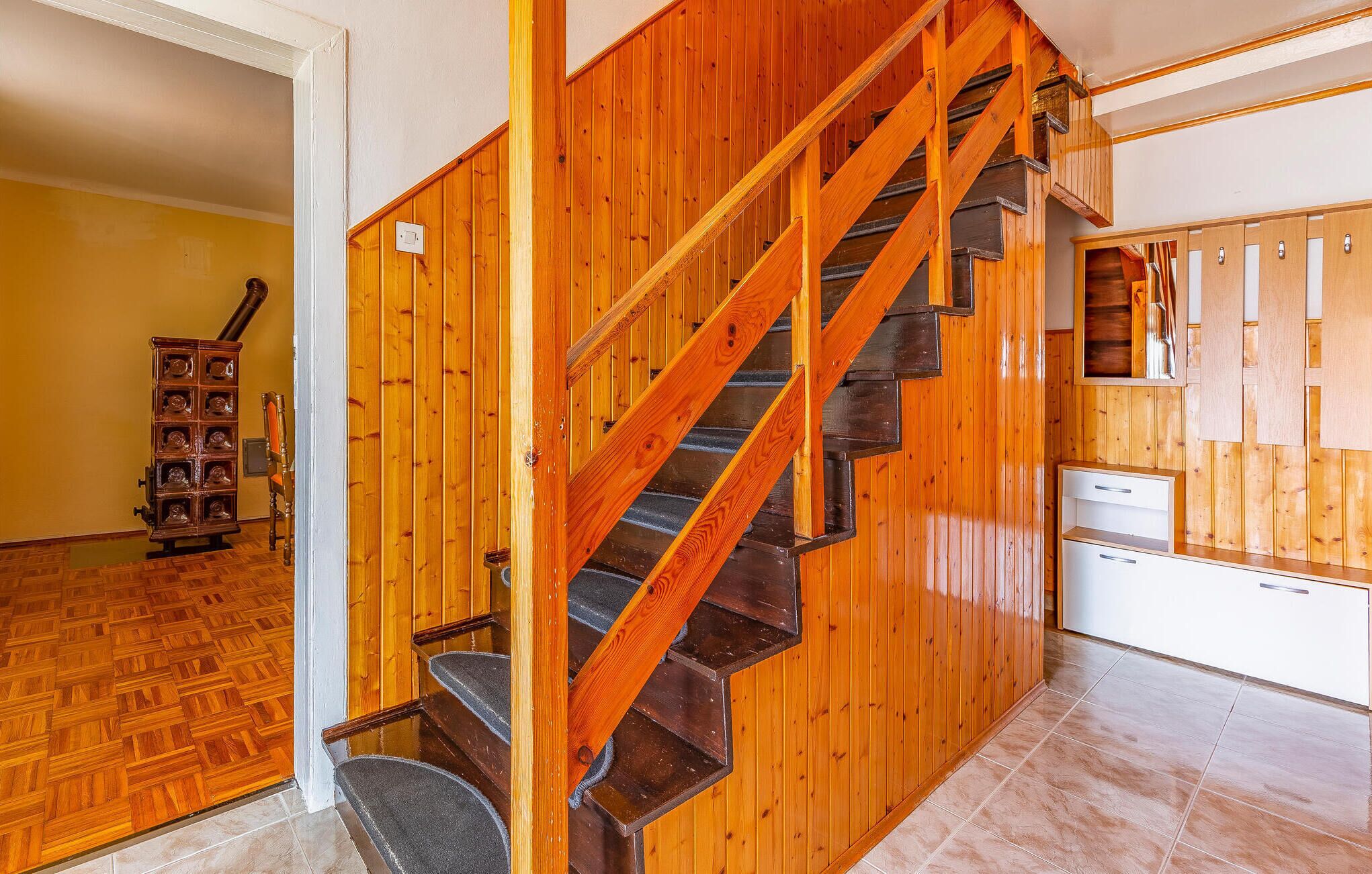 A wooden staircase with a handrail, a wooden cabinet with multiple drawers, and a tiled floor.
