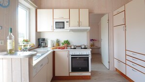 A compact kitchen with a microwave, oven, and sink. There is a bottle of wine and a clock on the wall. - Beach front home in Schönhagen (Schönhagen)