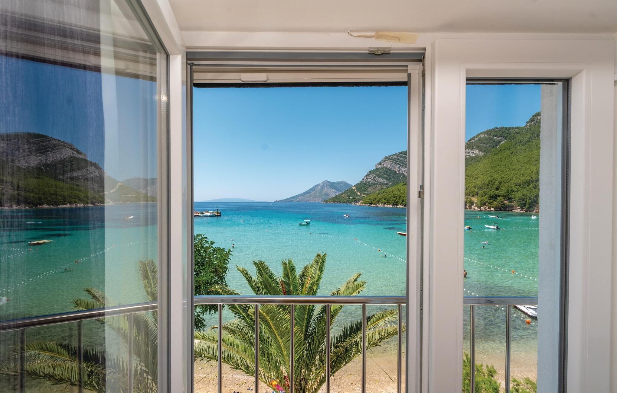 Un balcon offrant une vue dégagée sur une mer turquoise, des bateaux et un paysage montagneux.