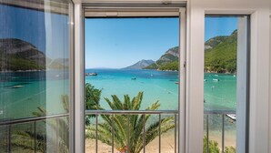 A balcony with a clear view of a turquoise sea, boats, and a mountainous landscape.