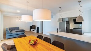 A modern living space with a dining area, sofa, TV, and kitchen.