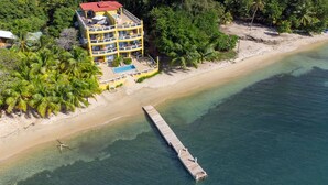 Ein mehrstöckiges Hotel mit Pool direkt am Strand, mit einem hölzernen Steg, der sich ins Wasser erstreckt.