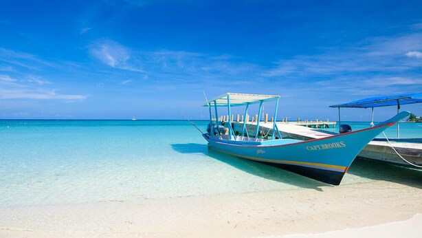 Ein Boot namens "Capt Brooks" liegt an einem klaren, türkisblauen Strand mit weißem Sand und blauem Himmel.