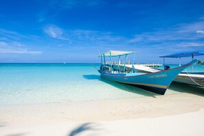 Ein Boot namens "Capt Brooks" liegt an einem klaren, türkisblauen Strand mit weißem Sand und blauem Himmel.
