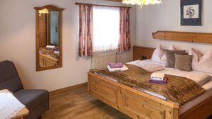 Un dormitorio acogedor con una cama de madera, un espejo, una ventana con cortinas, un radiador y una mesita de noche.