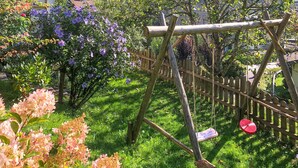 Un jardín con un conjunto de columpios de madera, una valla de madera y diversas plantas con flores.