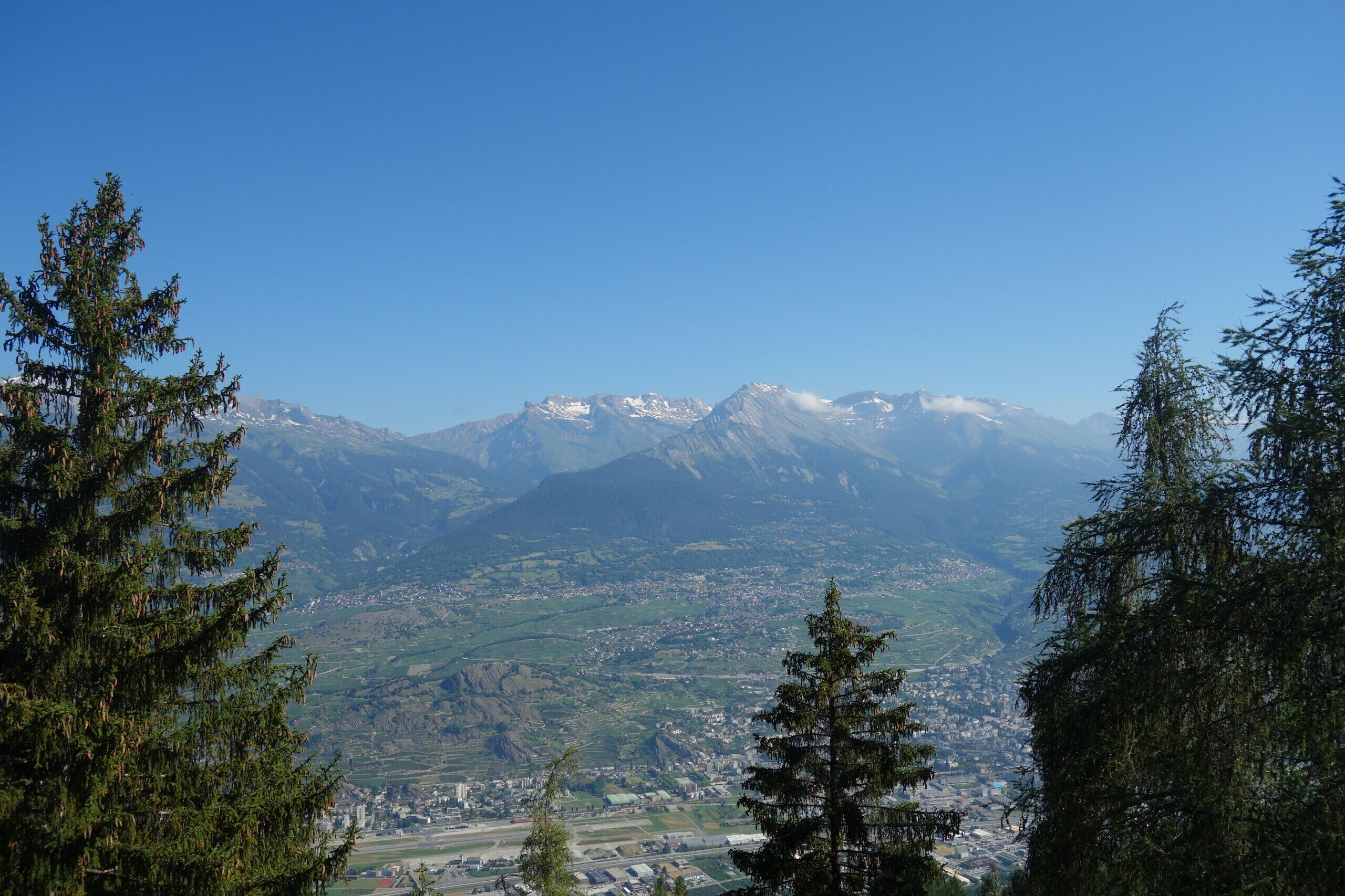 A mountainous landscape with snow-capped peaks and a valley with buildings and roads.