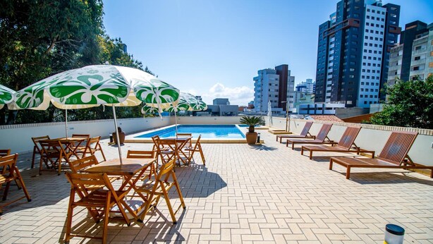 A rooftop pool area with lounge chairs and umbrellas, surrounded by high-rise buildings. - A Furninha Hotel (Torres)