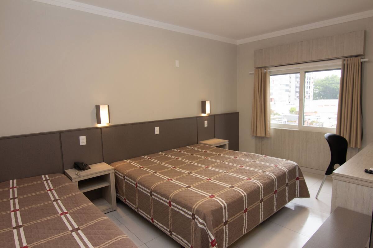 A hotel room with a large bed, a desk, and a chair. There are two bedside tables and a lamp on each side of the bed.