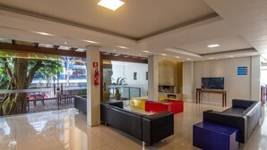 A modern lobby with a reception desk, seating area, and a television. - A Furninha Hotel (Torres)
