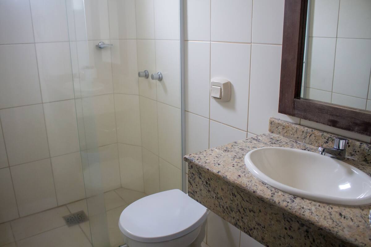 A bathroom with a glass shower enclosure, a white toilet, and a granite countertop with a sink.