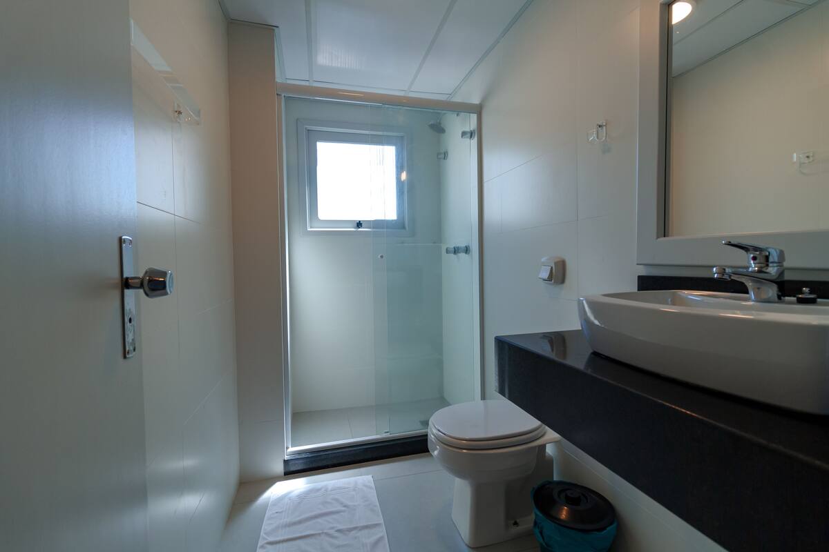 A modern bathroom with a glass-enclosed shower, a white toilet, and a large mirror above a sink.