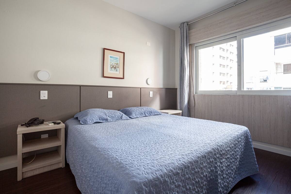 A hotel room with a large bed, bedside tables, a phone, and a window with a view of buildings.