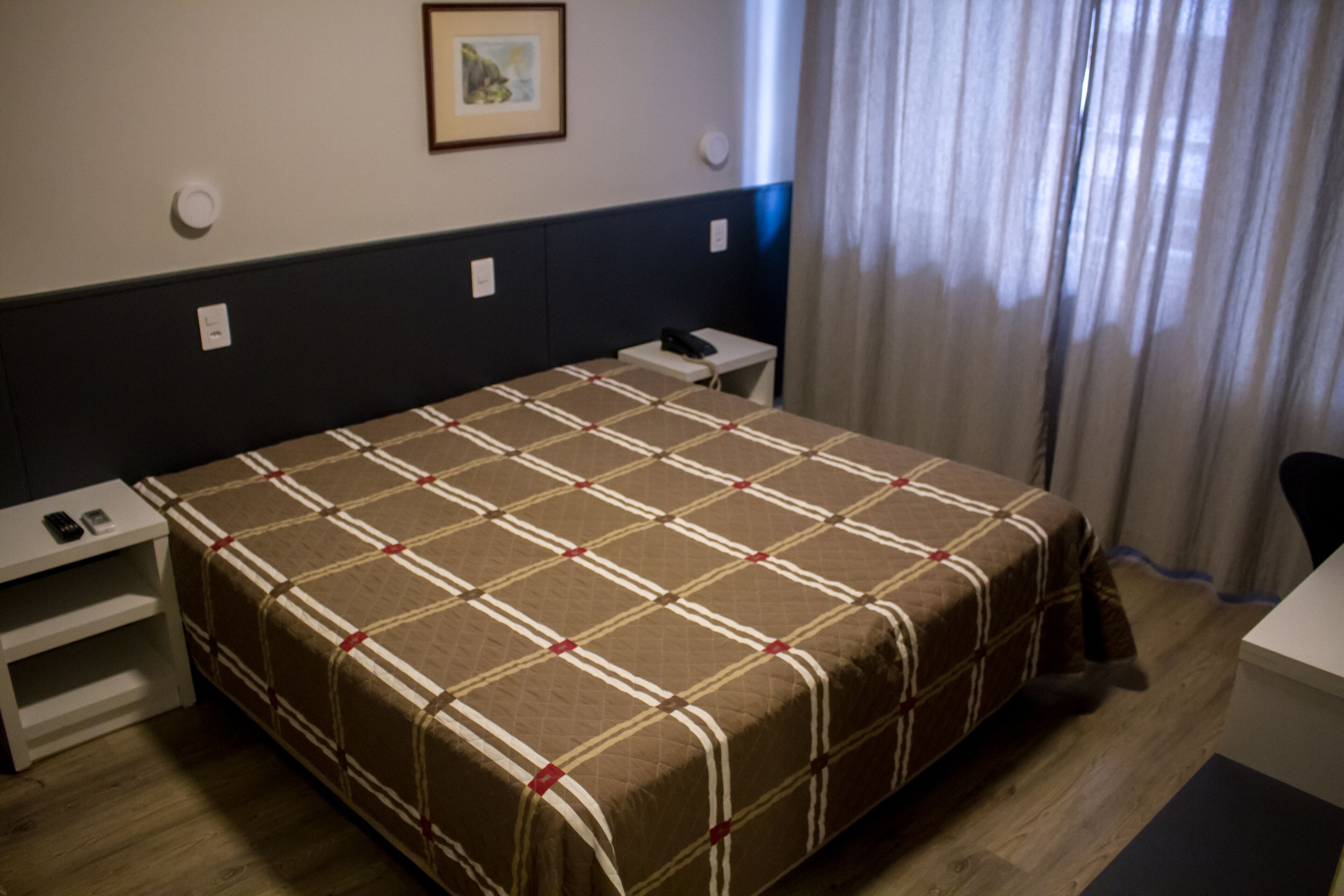 A hotel room with a large bed, a bedside table with a phone, and a small table with a lamp.