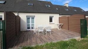 Una casa con terraza de madera, una puerta blanca y un ventanal pequeño.