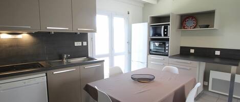 A modern kitchen with a dining area, featuring a dishwasher, stove, microwave, and oven.