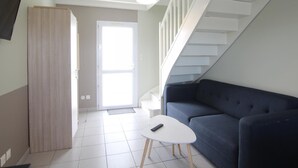 Una sala de estar moderna con un sofá azul oscuro, una mesa de centro blanca y una escalera con barandillas blancas.