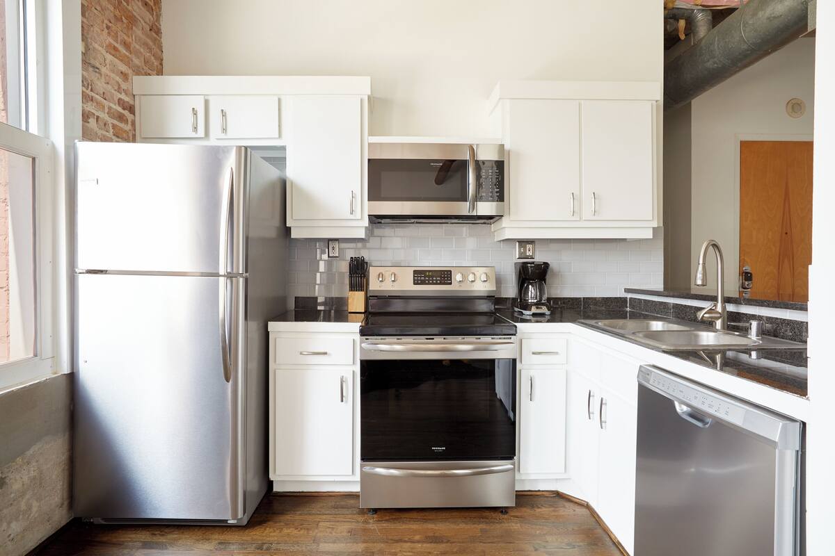 A compact kitchen with white cabinets, a stainless steel refrigerator, a microwave, an oven, and a dishwasher.