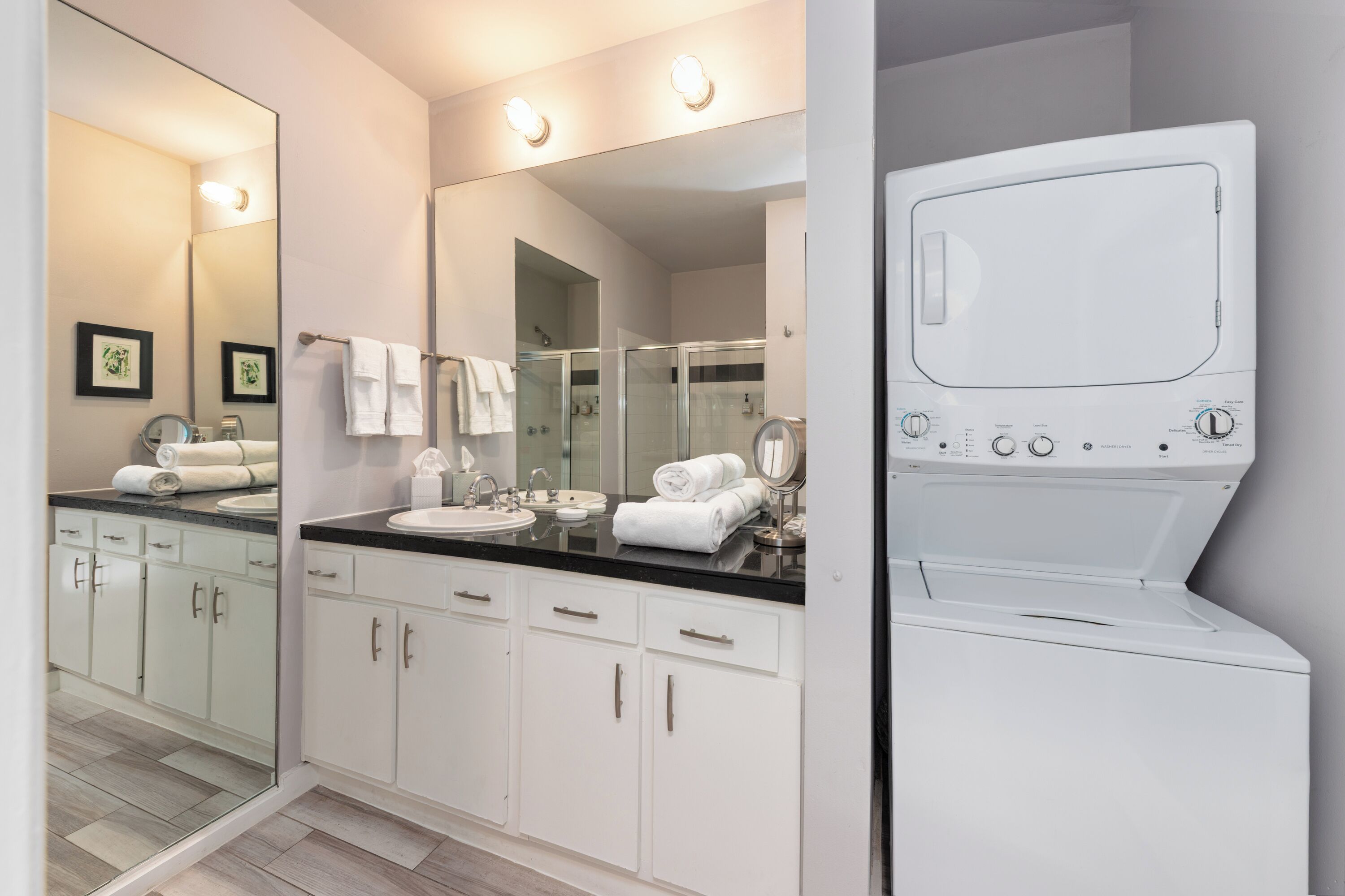 A modern bathroom with a large mirror, white cabinets, a black countertop, and a built-in washing machine.