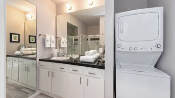A modern bathroom with a large mirror, white cabinets, a black countertop, and a built-in washing machine.