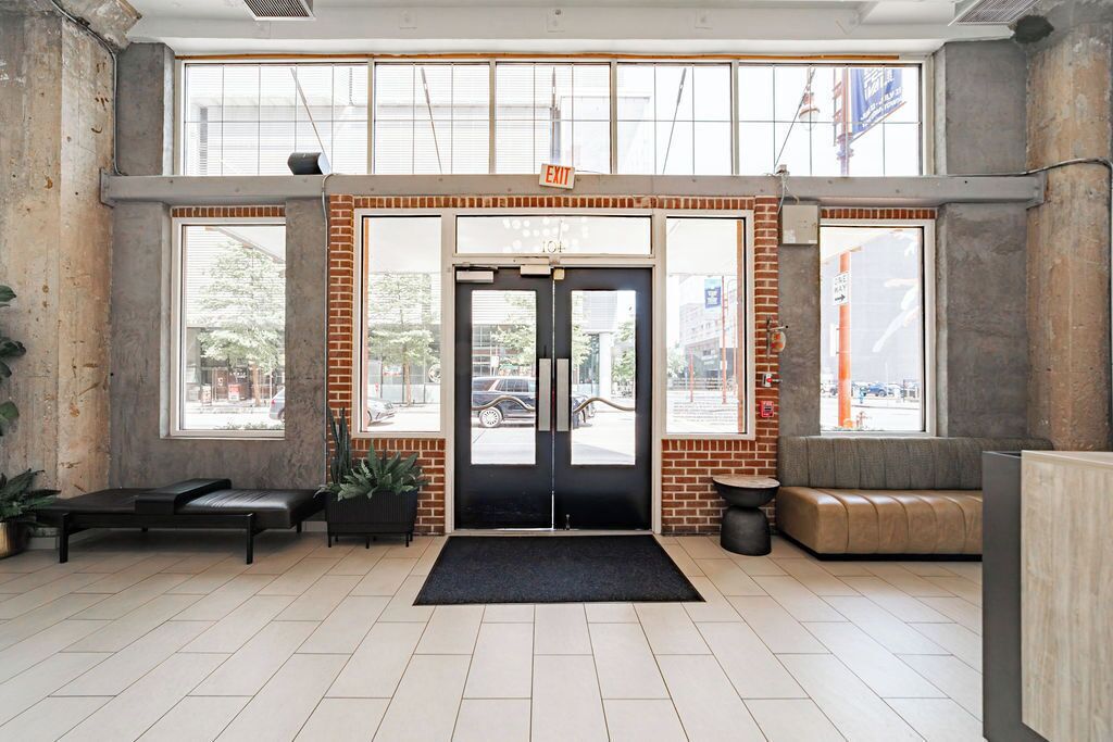 A modern lobby with a black double door, large windows, a black bench, and a grey sofa.