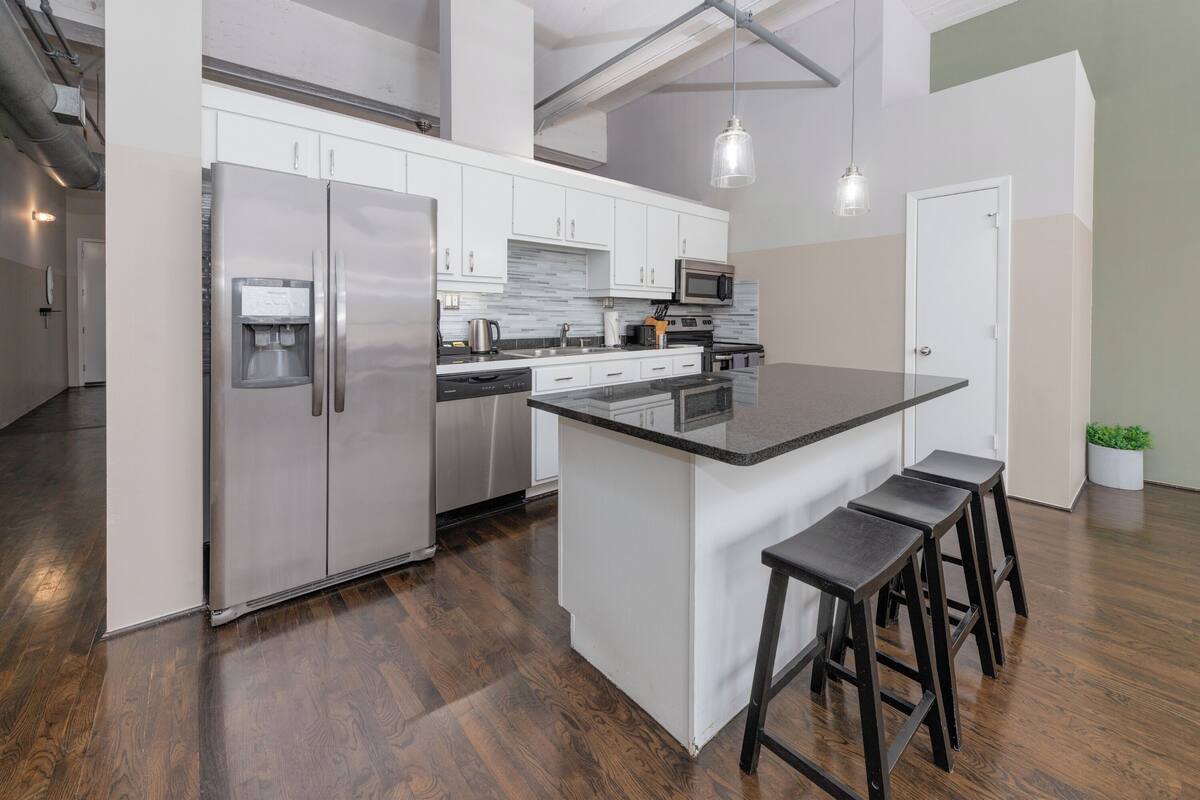 A modern kitchen with stainless steel appliances, a granite countertop, and wooden stools.