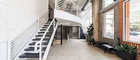 A spacious lobby with a curved staircase, seating area, and large windows.