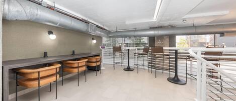Zona de bar moderna con taburetes altos, una barra alargada y vistas de la ciudad a través de amplios ventanales.