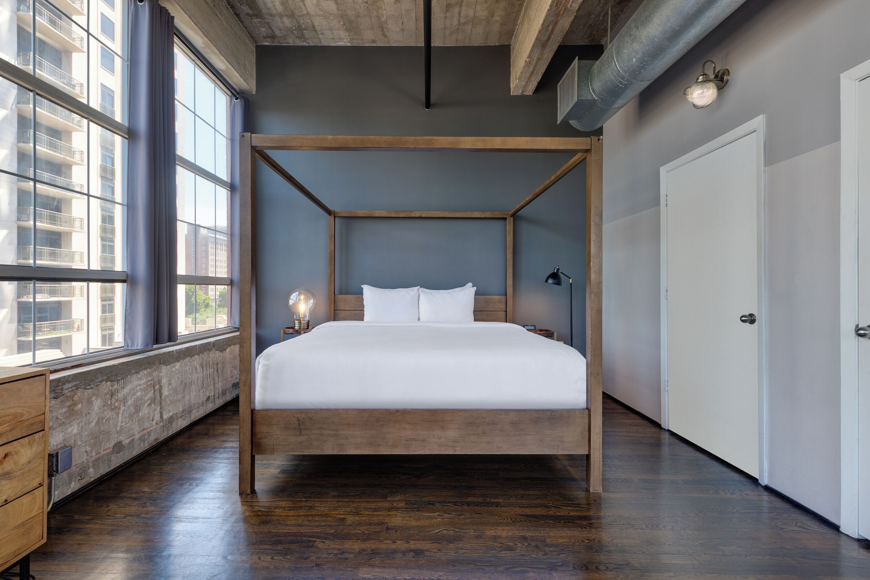 Ein modernes Schlafzimmer mit einem hölzernen Himmelbett, großen Fenstern und Blick auf Gebäude.