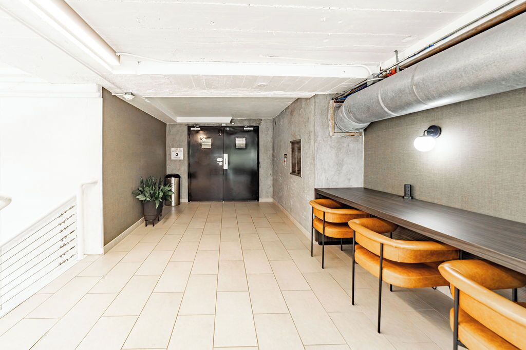 A corridor with a long table and chairs, a door with a sign, and a potted plant.