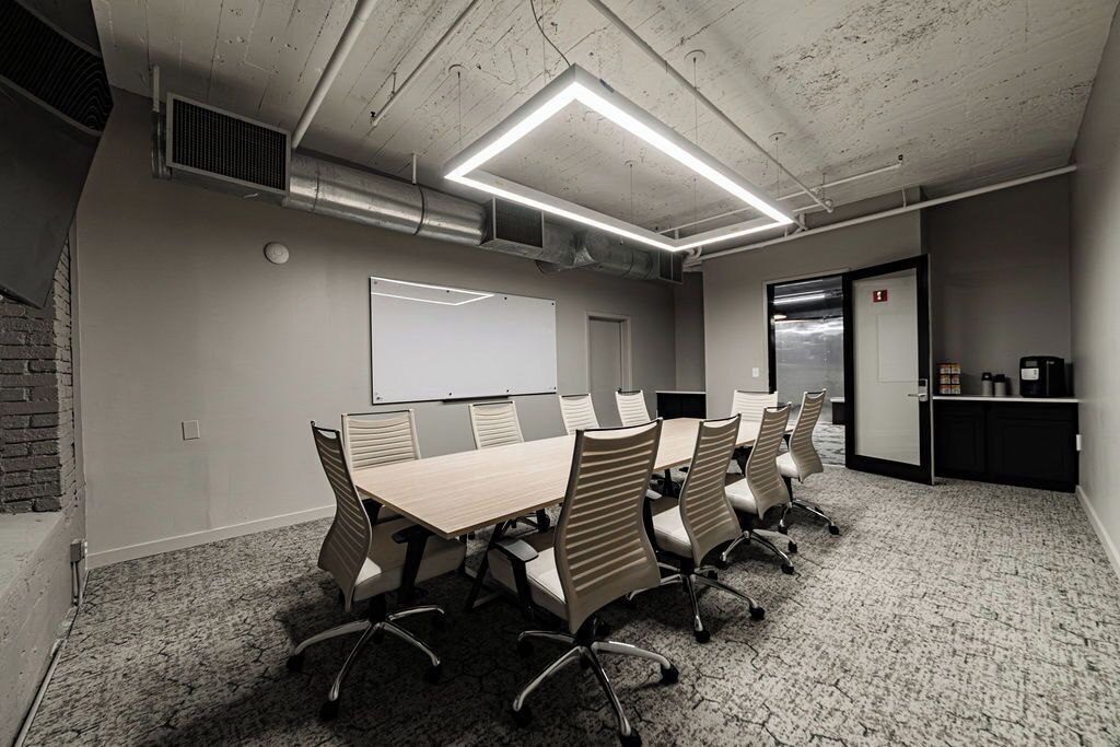 A conference room with a long table, six chairs, a whiteboard, and a door with an elevator.