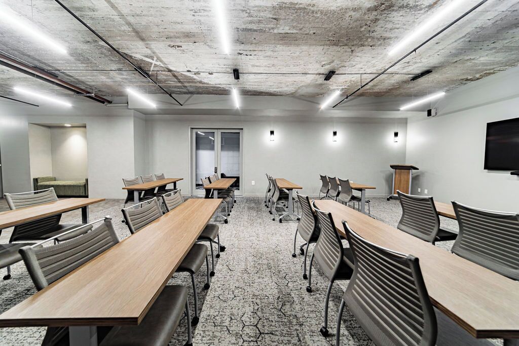 A conference room with long tables and chairs, a large window, and a flat-screen TV on the wall.