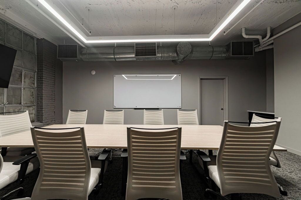 A conference room with a long table, six chairs, a whiteboard, and a door.