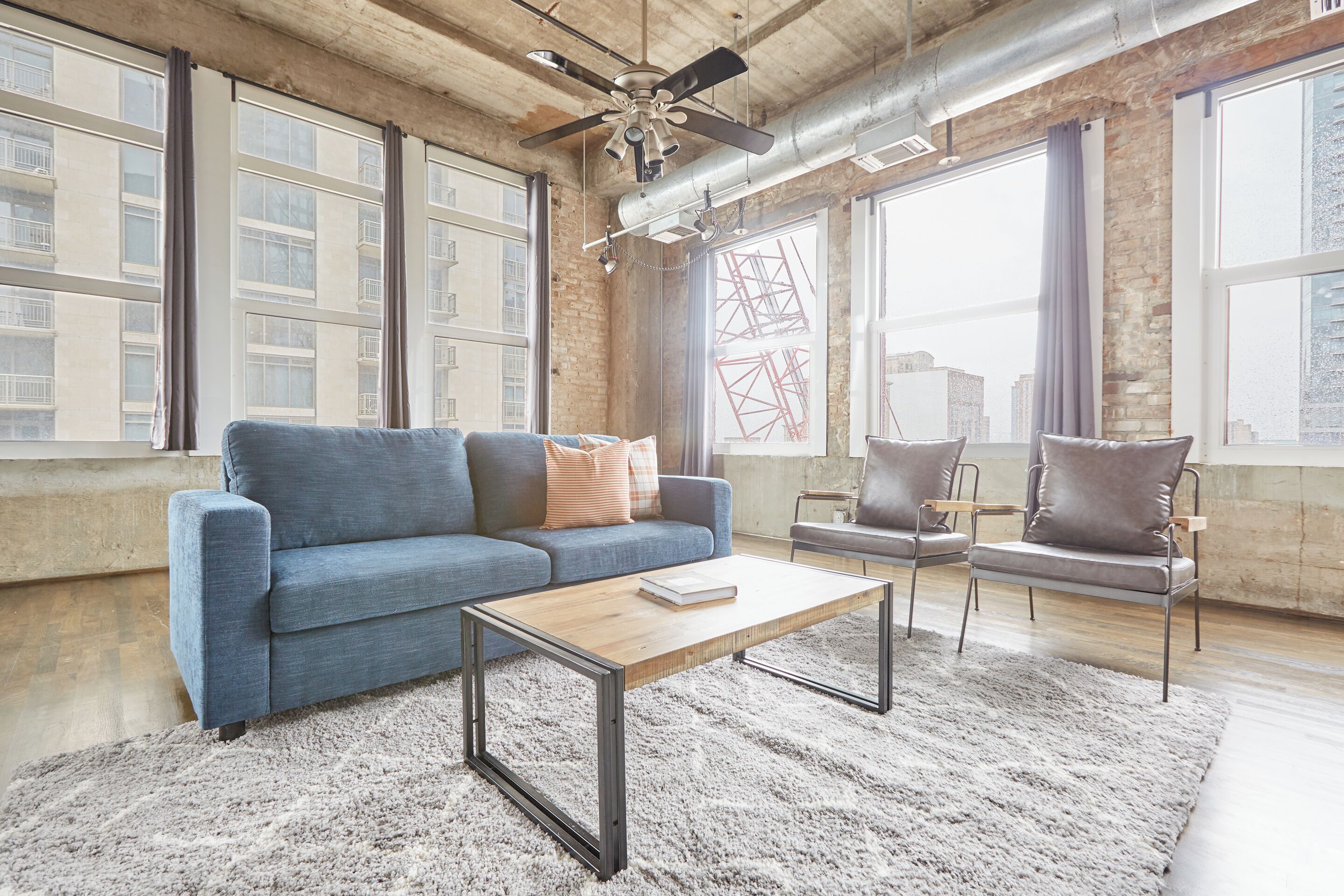 A modern living room with a sofa, armchair, coffee table, and large windows with a city view.