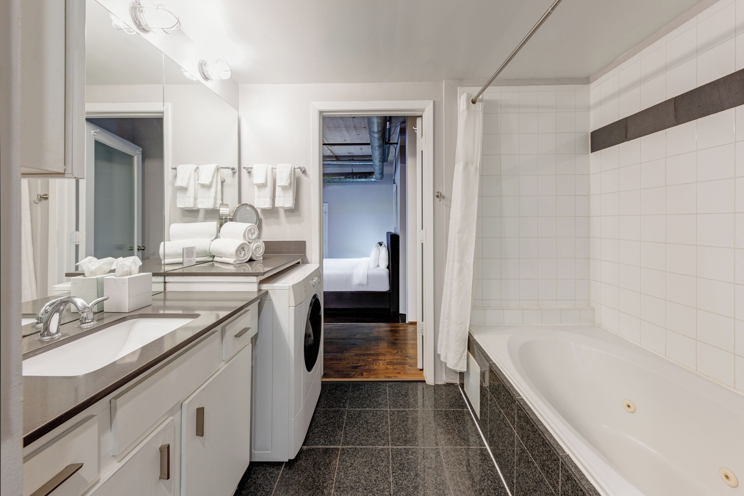 A modern bathroom with a large sink, a washing machine, a bathtub, and a shower area.
