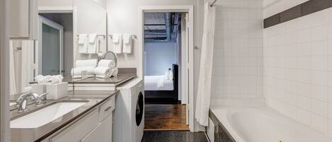 A modern bathroom with a large sink, a washing machine, a bathtub, and a shower area.