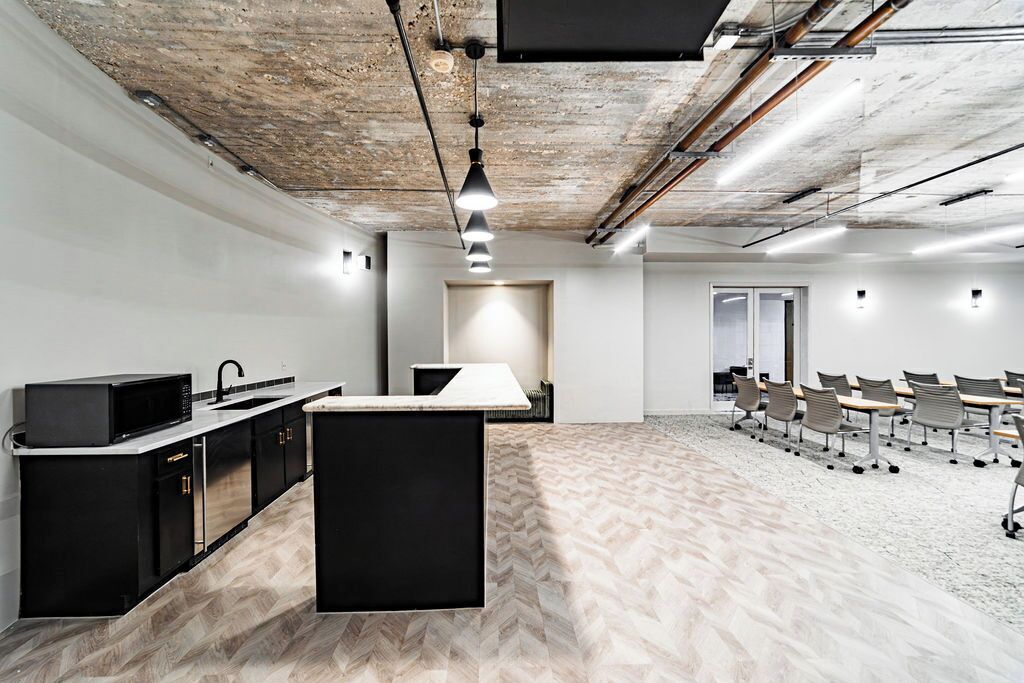 Un espacio de oficina moderno con una zona de cocina, una mesa de reuniones grande y un suelo con estampado de espiga.