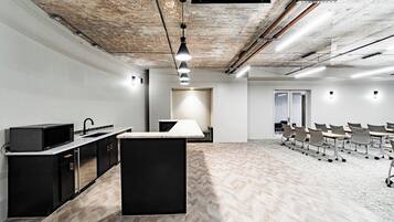 A modern office space with a kitchen area, a large meeting table, and a herringbone-patterned floor.