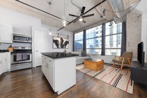 Une cuisine moderne avec des meubles blancs, un îlot central et un coin repas comprenant un canapé et une table basse en bois.