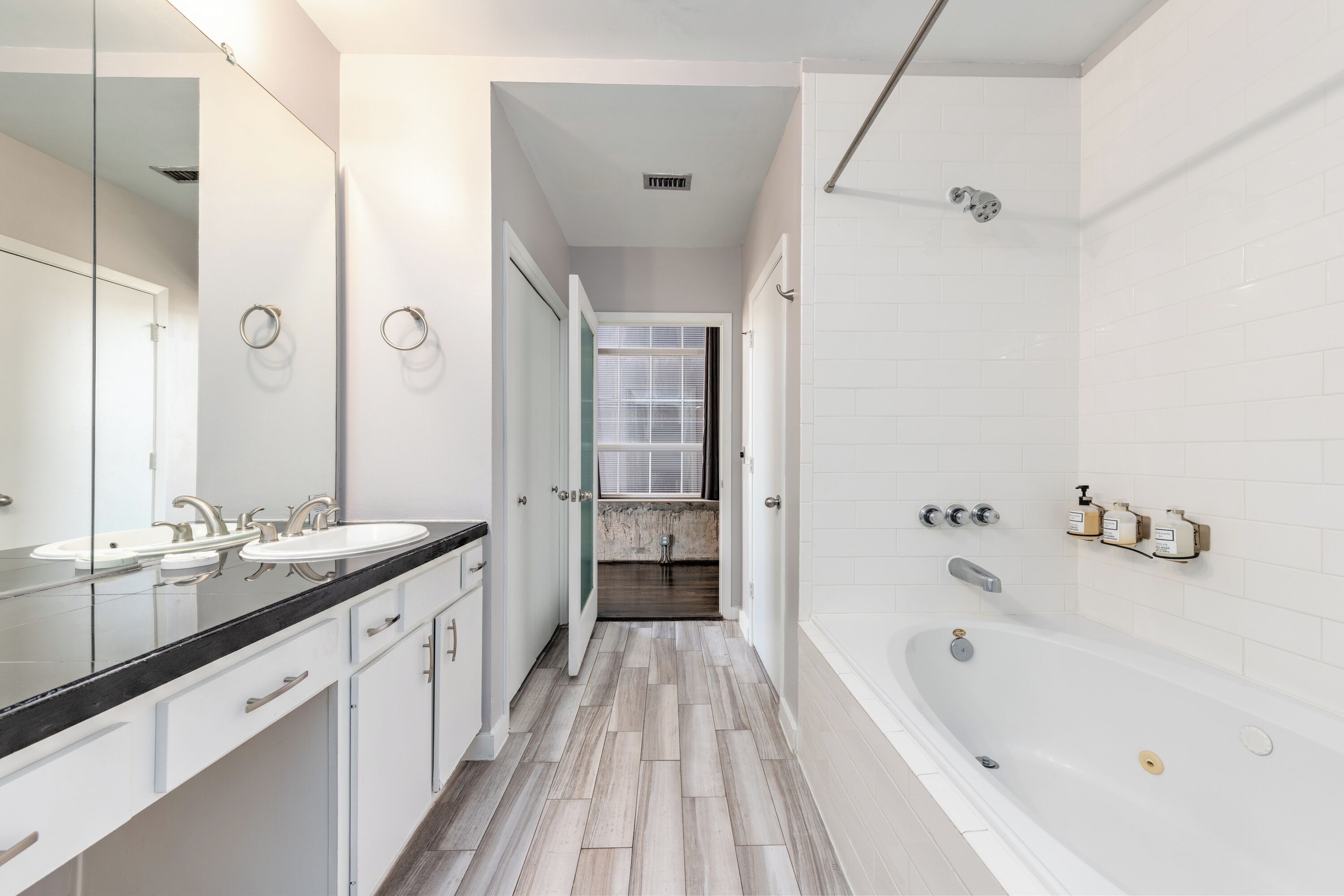 A modern bathroom with a large mirror, two sinks, a bathtub, and a shower.