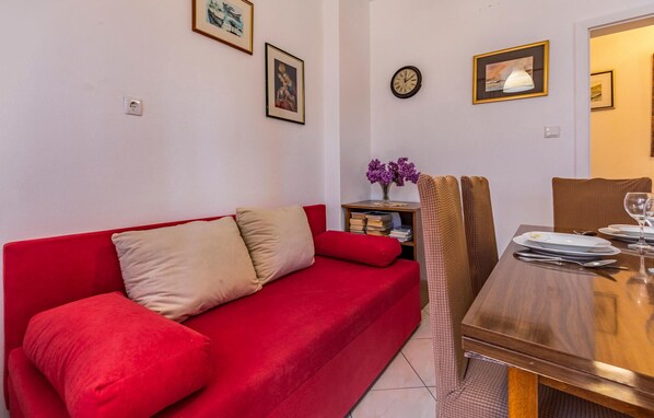 Un sofá rojo con cojines, una mesa de comedor de madera con platos y vasos, y un reloj de pared.