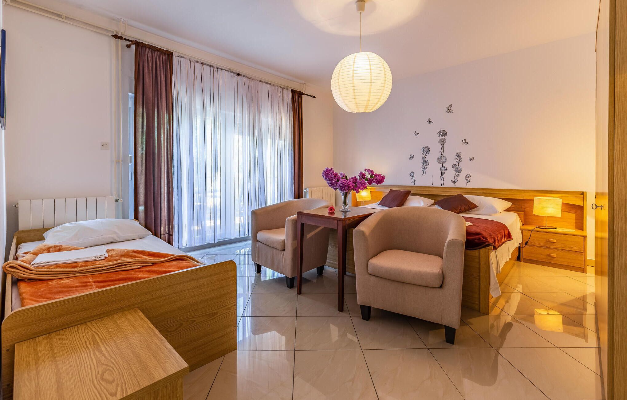 A hotel room with a bed, two armchairs, a small table with a vase of flowers, a lamp, and a wall with floral decals.