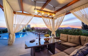 A poolside area with a glass table, lounge chairs, and a view of mountains at sunset. - Stunning home in Otok Dalmatinski (Otok Dalmatinski)