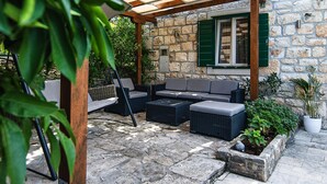 An outdoor seating area with a stone wall, green shutters, and a pergola. - Stunning home in Postira (Postira)