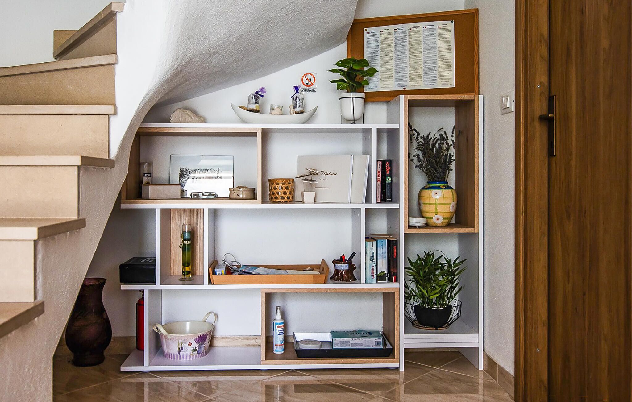 A staircase leading to a landing with a white shelving unit containing books, decorative items, and a potted plant.
